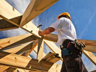 A person in a hard hat hammering a nail into a wooden beam