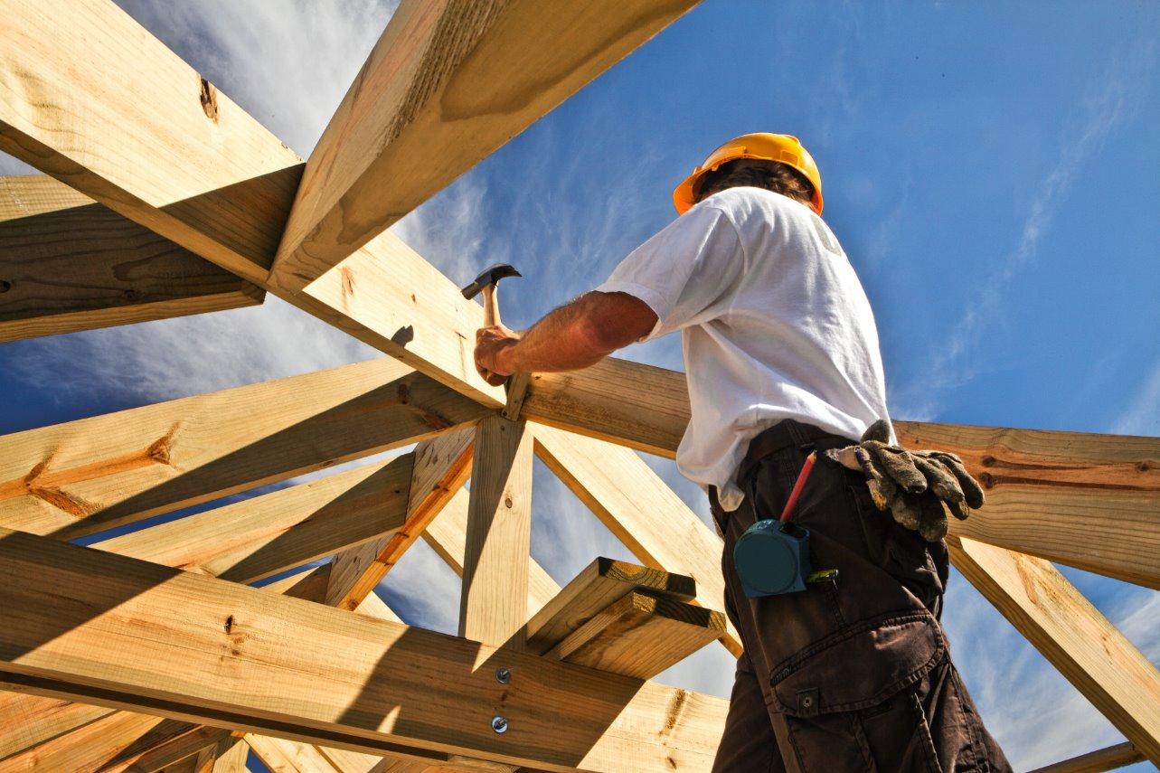 A person in a hard hat hammering a nail into a wooden beam
